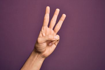 A hand is reaching into the frame of the photo and holding up three fingers to indicate the number 3.