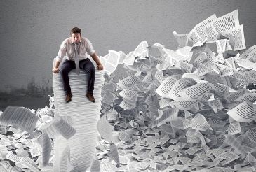 A businessman is sitting on top of a tall stack of papers and is surrounded by a huge heap of loose paper.