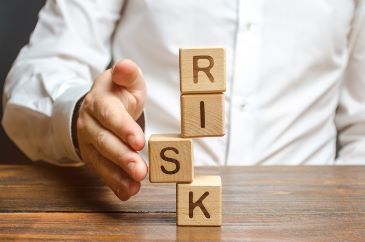 A person straightens a segment in an unstable tower of cubes labeled with the letters R I S K.